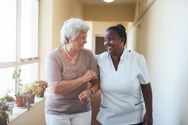 sorridente assistente domiciliar e mulher sénior a caminhar juntos - patient retirement senior adult hospital imagens e fotografias de stock