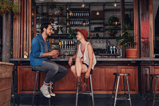 Young couple sitting at cafe counter Shot of young couple sitting at cafe counter. Young man and woman at coffee shop. bar stool photos stock pictures, royalty-free photos & images