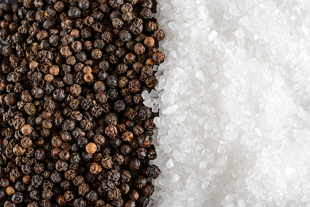 Close up of a stack of salt crystals and black peppercorns.