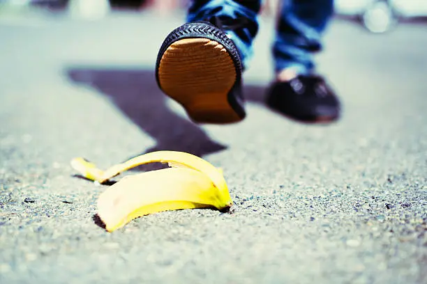 An unidentified  female walker's foot is about to step on a dropped banana peel - a painful accident waiting to happen! Focus on the sole of the shoe.