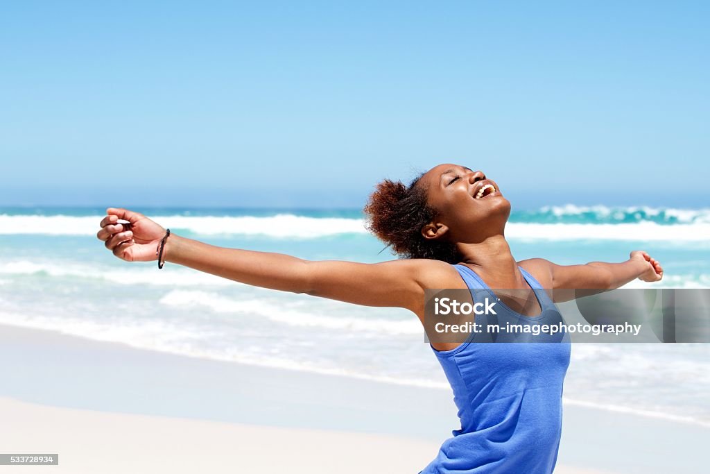 Carefree woman having a good time at beach Portrait of healthy young african woman standing on the beach with her hands outstretched Women Stock Photo