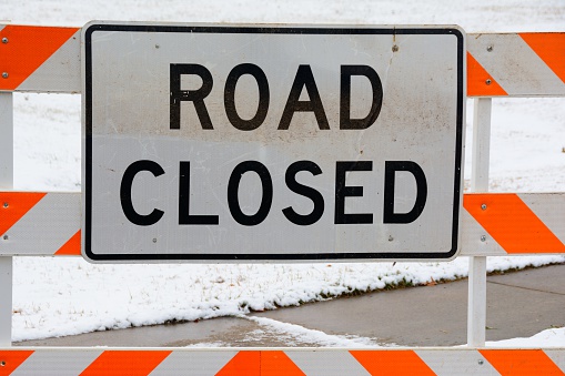 Photograph of a road closed sign placed in front of a snow covered area.