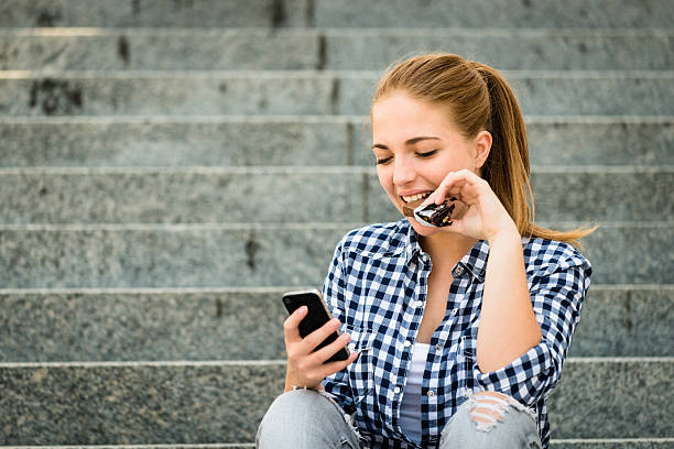 Adolescente comer chcolate olhando para telefone - fotografia de stock