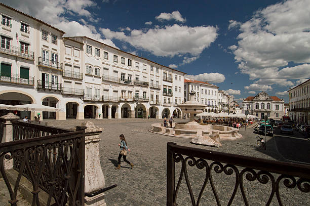 Evora, Portugal - May 3, 2013: Central square of Evora, Portugal. Fence in foreground, terraces, a woman passes by in the foreground.