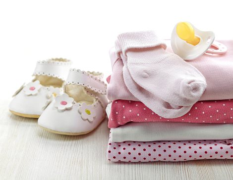 Pile of pink baby clothes and pacifier on white wooden background