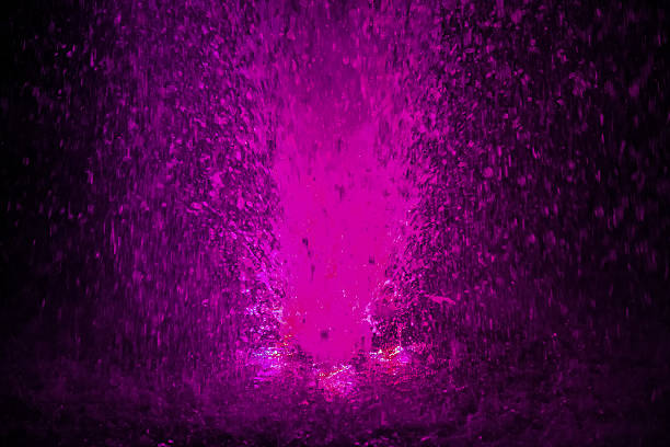 Colorful fountain splashes pink color of water drops on a black background