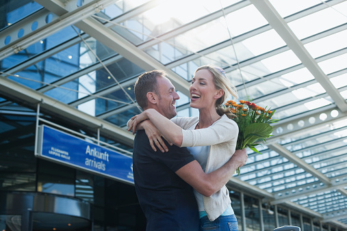 Germany, Leipzig-Halle, Airport, couple embracing man holding bunch of flowers