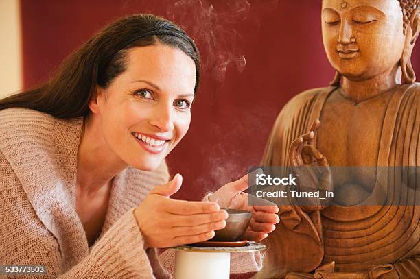 Brunette Woman Enjoying Joss Sticks Scent Buddha Statue In Background Stock Photo - Download Image Now