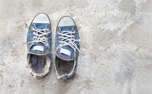 Old and dirty blue canvas sneakers on concrete floor