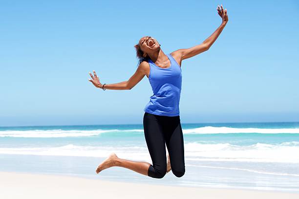 istock Young african woman jumping with joy at the beach 533833280