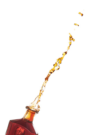 Bottle of Brandy popping its cork and splashing. Isolated on a white background