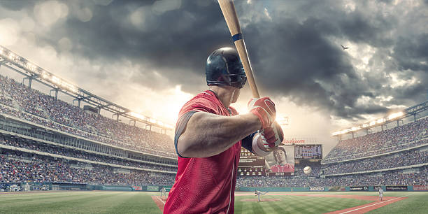 Rear View of Baseball Batter About to Hit During Game A close up rear view of a professional male baseball player wearing a red baseball strip and safety helmet, holding baseball bat just about to strike incoming baseball. The action occurs during a baseball game in a generic floodlit outdoor stadium full of spectators. Baseball ground, scoreboard etc are all fictional. batting sports activity photos stock pictures, royalty-free photos & images