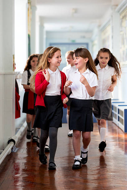 Schoolgirls Walking to Class Small group of schoolgirls walking to class wearing their school uniform. They all walk down a school corridor talking together. cardigan wales stock pictures, royalty-free photos & images