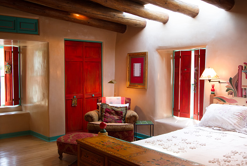 Santa Fe style: colorful rustic-chic bedroom with viga beams, thick adobe walls that are hand-troweled with a 