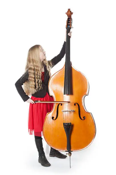 young blond girl in red dress plays double bass in studio against white background