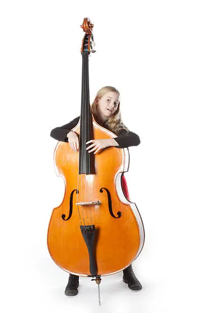 young blond girl in red dress holds double bass in studio against white background