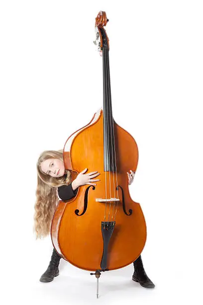 young blond girl looks from behind  double bass in studio against white background