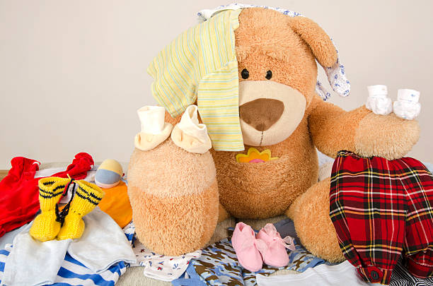 Bear toy on bed with different colorful new born clothes Bear toy on a bed with different colorful new born clothes.Colorful wardrobe of newborn,kids, babies full of all clothes, shoes,accessories and toysBear toy on a bed with different colorful new born clothes.Colorful wardrobe of newborn,kids, babies full of all clothes, shoes,accessories and toys baby boutique stock pictures, royalty-free photos & images