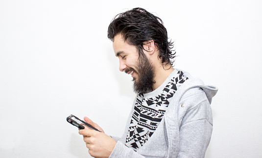 Portrait of smiling young man using digital tablet over white background. Teenage boy smiling isolated on white looking at digital tablet with happy facial expression. Young man has got medium length, black hair. Horizontal composition. Image developed from RAW format. Close-up portrait.