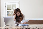 Worried woman looking at bills next to Macbook in kitchen