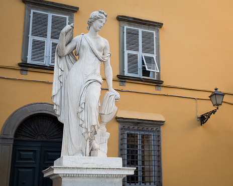 Ancient statue of a female figure with an amphora atop a water fountain in Piazza Salvatore in the Tuscan village of Lucca, Italy.