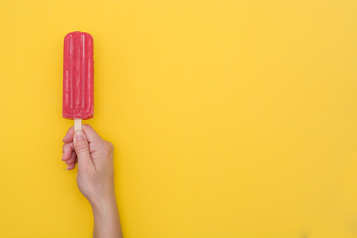 Strawberry popsicle in hand on yellow background