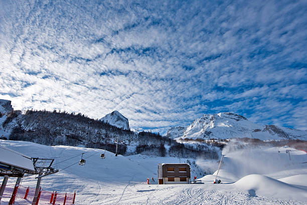 Its Morning time in Gourette winter sport resort in French Pyrenees Mountains. The Snow lances works along ski slopes. Sun lights a part of landscape. Cloud patterned sky is at background