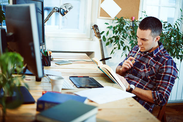 istock Young man in home office reading book 533886959
