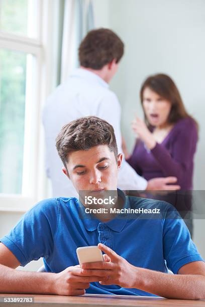 Teenage Boy Texts On Phone As Parents Argue In Background Stock Photo - Download Image Now