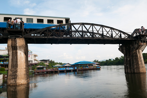 Kanchanaburi, Thailand - October 3, 2011: People step out of the way as a train crosses the famous Bridge on the River Kwai in Kanchanaburi, Thailand. The bridge was built by Allied prisoner of war labor during World War II.