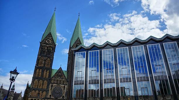 Bremen, Germany. Part of Parliament of Bremen and towers of Bremen Cathedral (German: 'Bremer Dom') on a sunny day. Partly cloudy sky mirrored in the huge glass front of the government building.