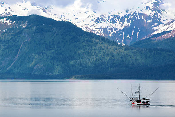 Fishing Trawler close to Glacier Bay National Park and Preserve, Alaska.  The Fishing Trawler is dwarfed by the bay and the mountains. Blue sea, sky and clouds.