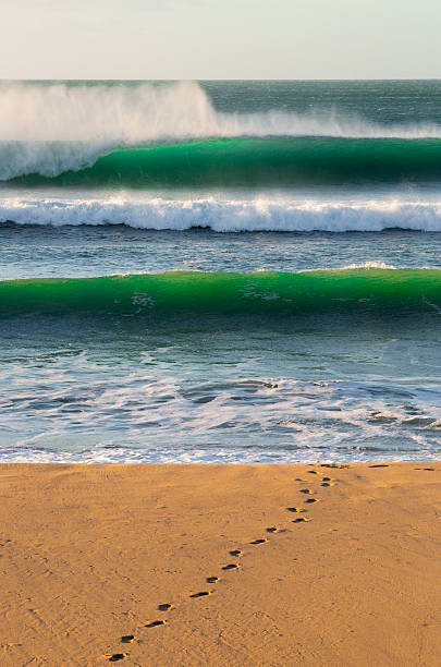 Surfer footprints on sandy beach with green waves breaking at Wainui Beach, Gisborne, New Zealand