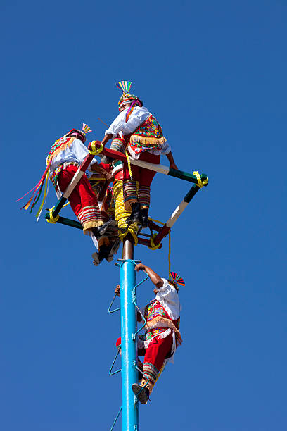 The Voladores of Tulum, Mexico Tulum, Mexico - November 16, 2015: The voladores, or flyers, of Tulum dress in brilliantly colored traditional costumes, climb up a very high pole (about 100 feet) tie their waist to ropes wound around the pole and then jump off, "flying" gracefully around and around the pole as the ropes unwind until they reach the ground. Slight motion blur on performers showing the action. volador stock pictures, royalty-free photos & images