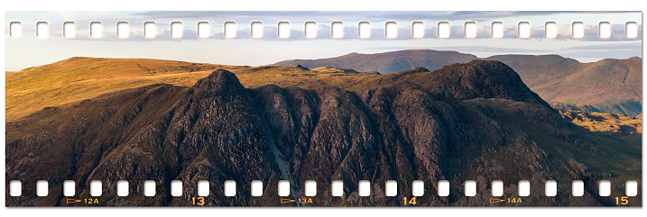 Panoramic image of the Langdale Pikes, in the English Lake District at sunset. The image is layered on a film strip, emulating certain cameras that can expose a film across its full width, including the perforation. My own image and background.