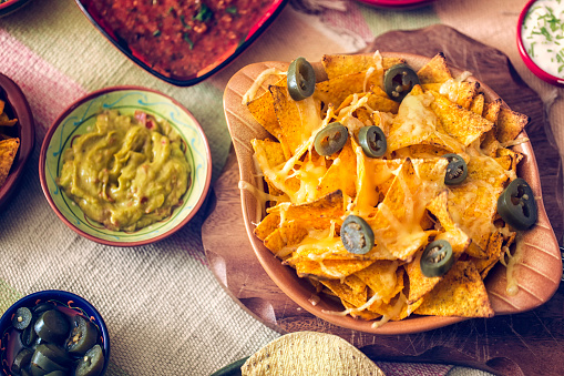Nachos, Mexican food, tortilla chips with beef and fresh vegetables, top shot on a black slate background with limes and guacamole dip