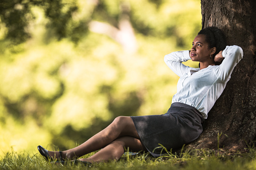 Mid adult African American businesswoman sitting in nature with hands behind her head and day dreaming.