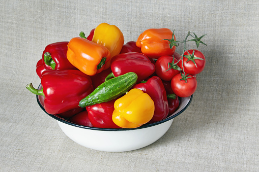 Red, yellow and orange paprika, tomato and cucumber lies in a basin