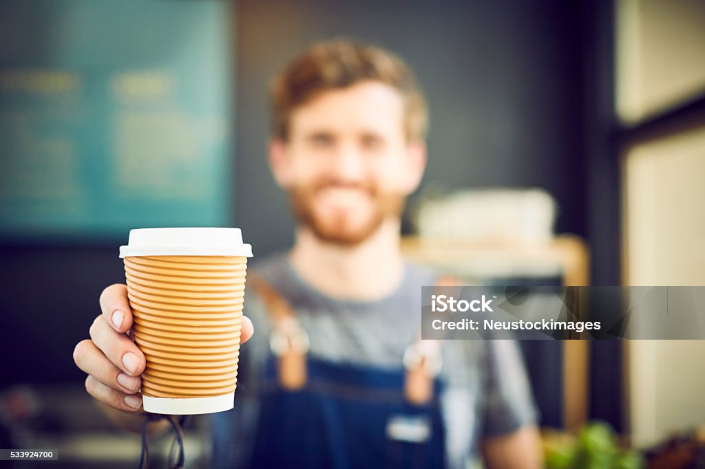 Barista offering coffee in disposable cup Young barista offering coffee in disposable cup. Smiling waiter is serving drink in coffee shop. Focus is on container. Coffee - Drink Stock Photo