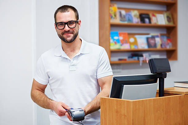 Salesman at the checkout in a bookstore Young salesman at the checkout in a bookstore book bookstore sale shopping stock pictures, royalty-free photos & images