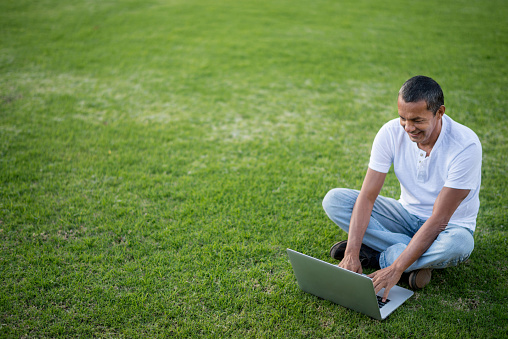 Man using a laptop outdoors sitting on grass