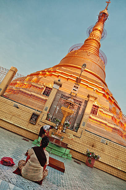 Yangon, Myanmar - February 24, 2011 : Burmese people sitting on the ground and praying in front of Botataung Pagoda in Yangon at sunset