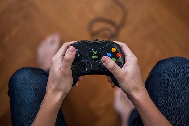 Xbox game controller - Microsoft Xbox Gothenburg, Sweden - January 24, 2015: A shot from above of a young mans hands holding a game controller for the Microsoft Xbox, a video game console. Natural lighting. Shot on wooden background with shallow depth of field.  brand name games console stock pictures, royalty-free photos & images