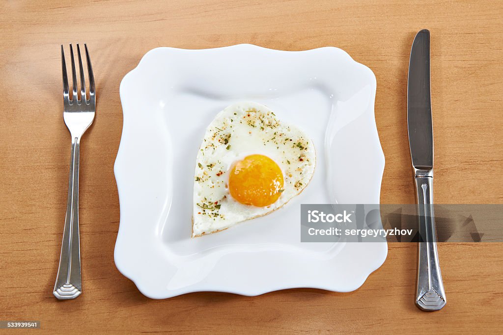 Fried eggs in heart shape on white plate and cutlery Table setting fried eggs in a heart shape on a white plate and cutlery 2015 Stock Photo