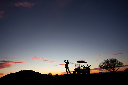 A male caucasian golfer swinging a golf club at dusk. Image taken in Arizona, United States, Canada at a premier golf course.