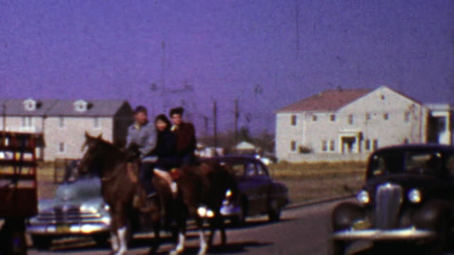 1955: Family crossing street riding horse as classic car drives by.