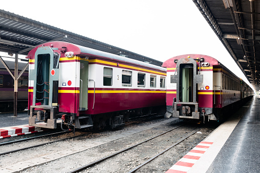 In Bangkok, Thailand historic Hua Lamphong railway station is the main hub to catch trains. Two regional trains with red, white and yellow stripes are parked at the platform. Photographed with a Nikon D800.