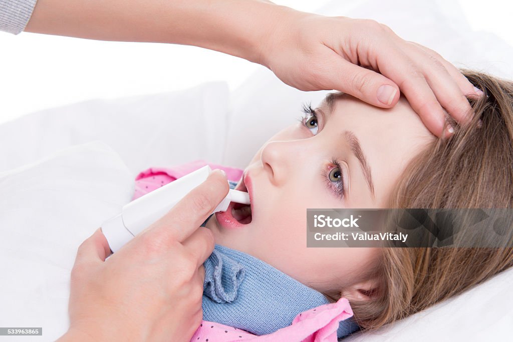 Little girl with sore throat using spray. Little girl with sore throat lying in bed and using spray on white background. 2015 Stock Photo