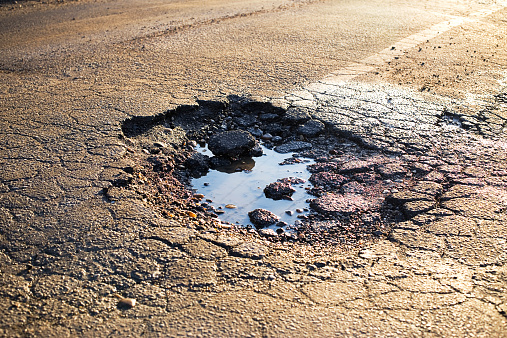 A road damaged by rain and snow, that is in need of maintenance. Broken asphalt pavement resulting in a pothole, dangerous to vehicles.