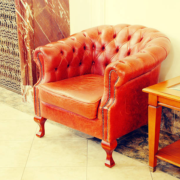 A plush orange recliner stands out in a minimalist room with white walls and a wooden rack
